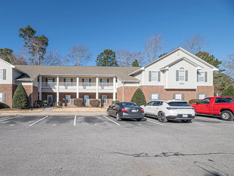 Two-story brick and white siding condo building with a long front balcony and a parking lot under a clear blue sky at 2221 Locksley Woods Dr Apt G, Greenville, NC 27858