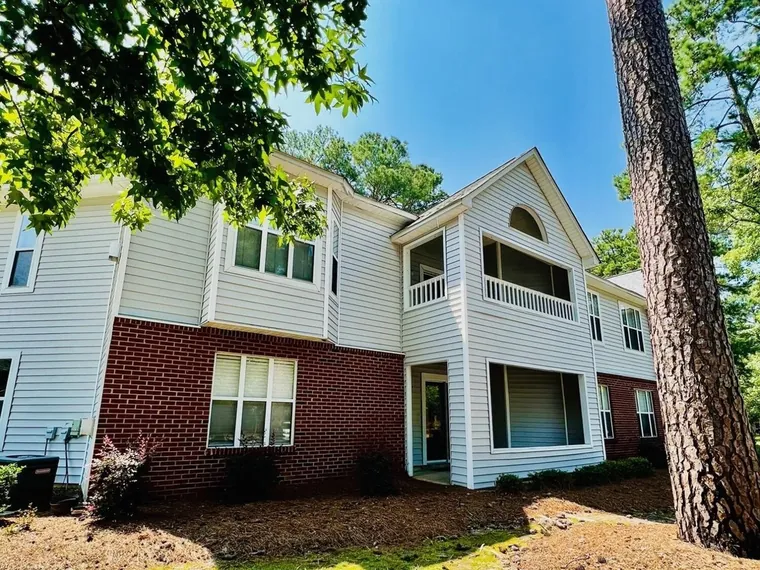 Two-story brick and white siding condo building with screened balconies among tall pines at 3302 Mulberry Ln Apt H, Greenville, NC 27858